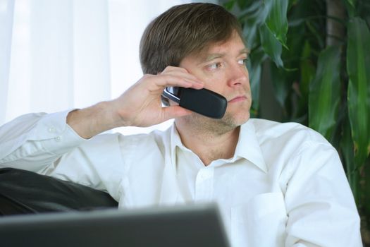 Handsome businessman working on laptop and using cell phone in casual attire.