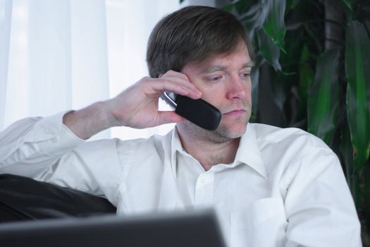 Handsome businessman working on laptop and using cell phone in casual attire.