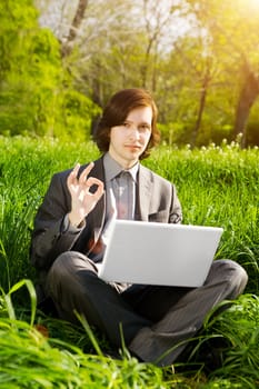 a young business man with a laptop on the grass field in sunset