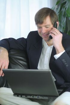 Handsome businessman working on laptop and using cell phone