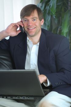 Handsome businessman working on laptop and using cell phone