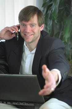 Handsome businessman on laptop and cell phone ready for handshake.