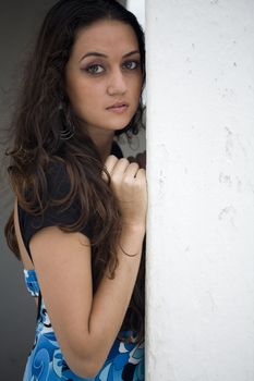 A young brazilian brunette wearing a blue dress next to a white wall.