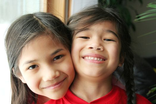 Two girls hugging and smiling. Part Scandinavian, part asian.