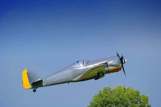 A light aircraft taking off into a clear blue sky, passing above a tree in the background. Motion blur on the propeller. Space for copy in the sky.