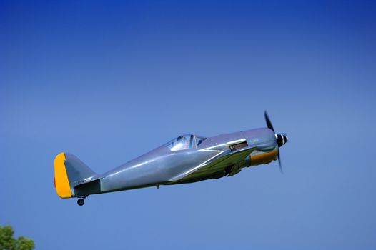 A single-seater aircraft taking off into a clear blue sky. Space for text in the sky.