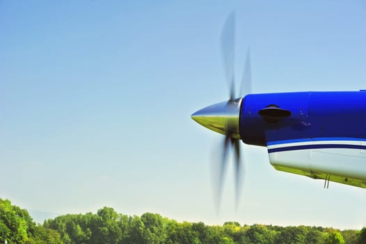 The propeller of an aircraft starting up, with motion blur on the blades. Space for text in the sky.