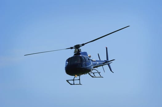 Partial silhouette of a helicopter coming in to land against a clear blue sky, landing light on.