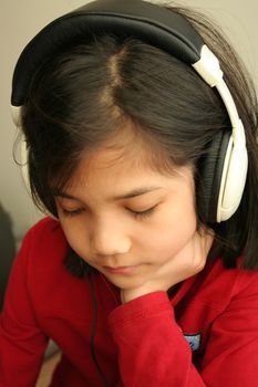 Child with sad expression listening to music on the headphones. Part asian, scandinavian descent.