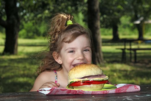 hungry little girl eat big sandwich in park