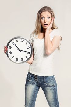 Surprised attractive young woman holding big clock