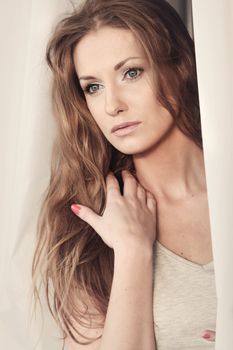 Beautiful girl looking through the curtains