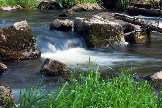 spring flowing brook, detail flowing water between stones and grass