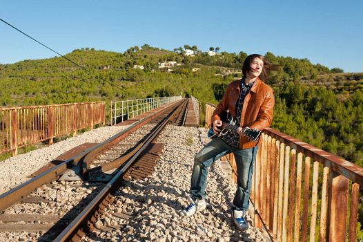 Young guitarist playing on a rusty railway bridge