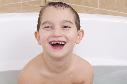 Happy kid is smiling in the bathtub while his hair wet.