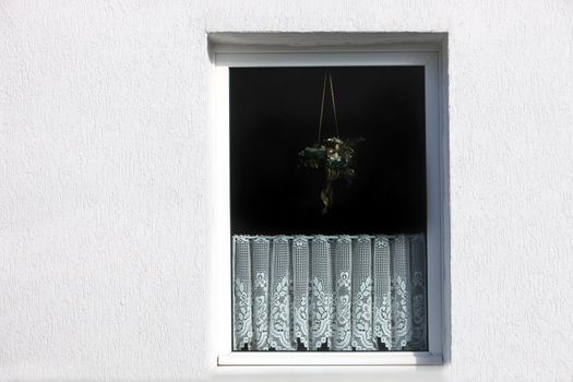 Outside view of a window in a white exterior wall of a house with a decorative net curtain on the lower half