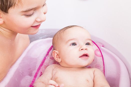 Pretty baby girl is having a bath in her bathtub with her, brother.