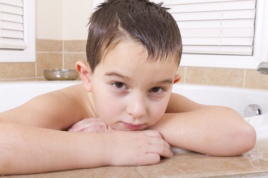 Seven years old kid looking at you pensively from a bath tub.