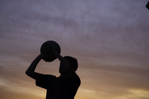 boy shooting basketball silhouette with a sunset in background