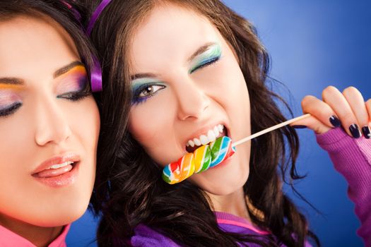 Close-up of two beautiful girls - one of them giving a blink and biting lollipop