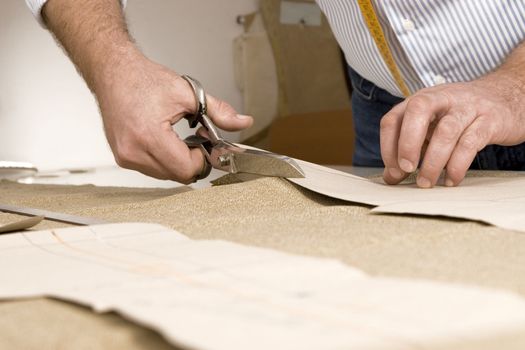 Tailor working at studio cutting fabric, detail of hand with scissors