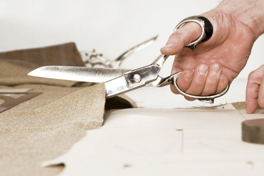 Tailor working at studio cutting fabric, detail of hand with scissors