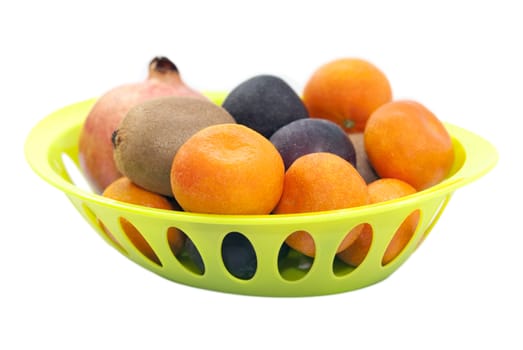 Mandarins, pomegranate, plums and kiwi fruits in the green plate isolated on white background