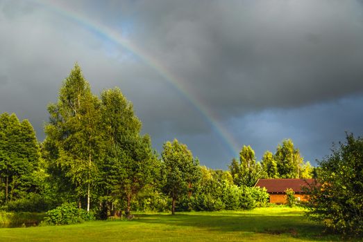 Real rainbow against a stormy sky in a beautiful green countryside in summer