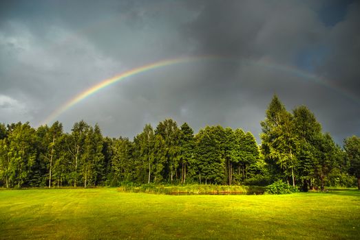 Real rainbow against a stormy sky in a beautiful green countryside in summer