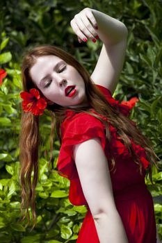 Beautiful model with white skin wearing a red dress with green foliage in background