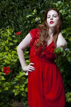 Beautiful model with white skin wearing a red dress with green foliage in background