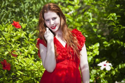 Beautiful model with white skin wearing a red dress with green foliage in background