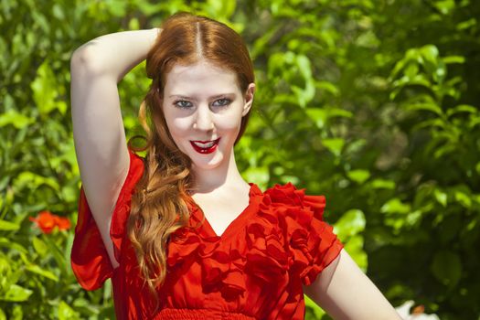 Beautiful model with white skin wearing a red dress with green foliage in background