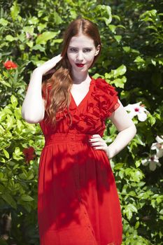 Beautiful model with white skin wearing a red dress with green foliage in background