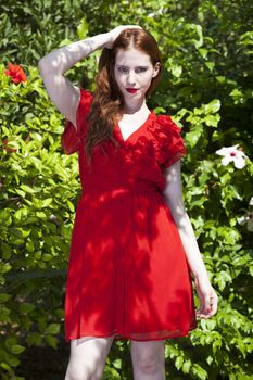 Beautiful model with white skin wearing a red dress with green foliage in background