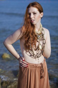 Beautiful woman with pale skin and long red hair semi-nude on a beach