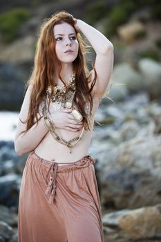 Beautiful woman with pale skin and long red hair wearing Bohemian jewellery and posing semi-nude on a beach