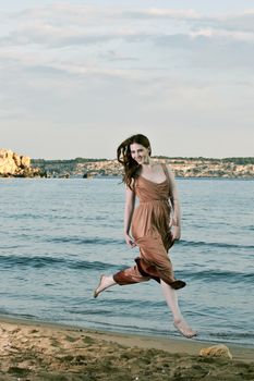 A young female model and dancer jumps and dances on a Mediterranean beach