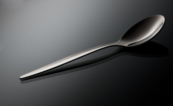 empty shiny silver spoon  on black reflective surface