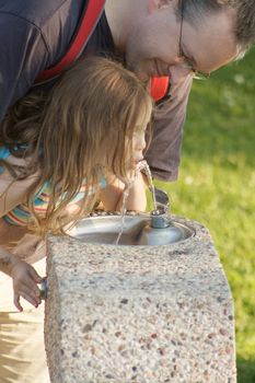 Father helping his daughter to drink from a fountain