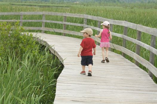 Brother and sister walking on a wooden sidewalk in a marsh