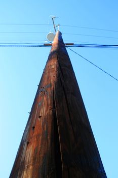 Close up of a telephone pole over blue sky.
