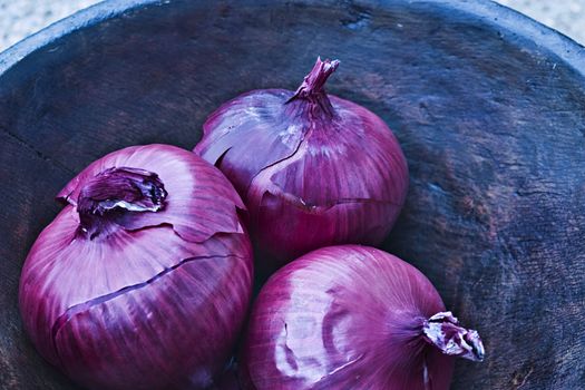 Red onions in a hand carved wooden bowl.