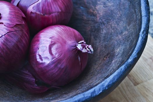 Red onions in a hand carved wooden bowl.