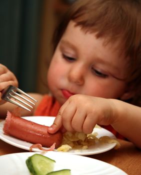 The small child eats sausage with macaroni. The foreground in a zone of sharpness, the rest is dim