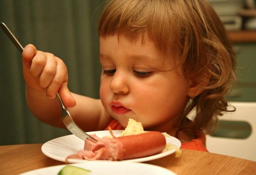 The small child eats sausage with macaroni