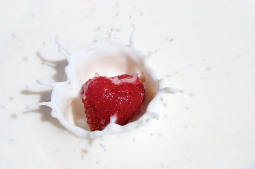Small strawberry splashing into cold milk