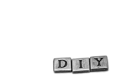 Metal scrapbooking letters spelling DIY: Do It Yourself. They lay on a white background.