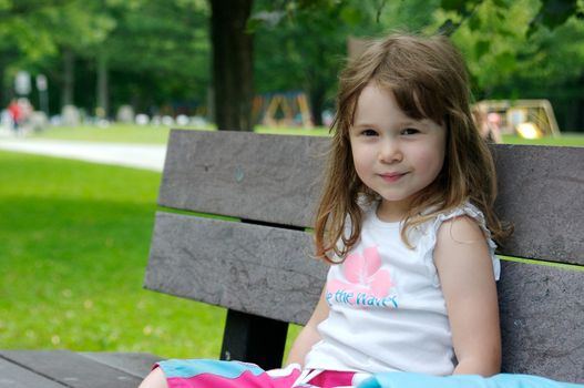 A cute little girl sitting on a park bench and smiling