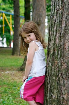 Cute little girl standing against a tree and smiling
